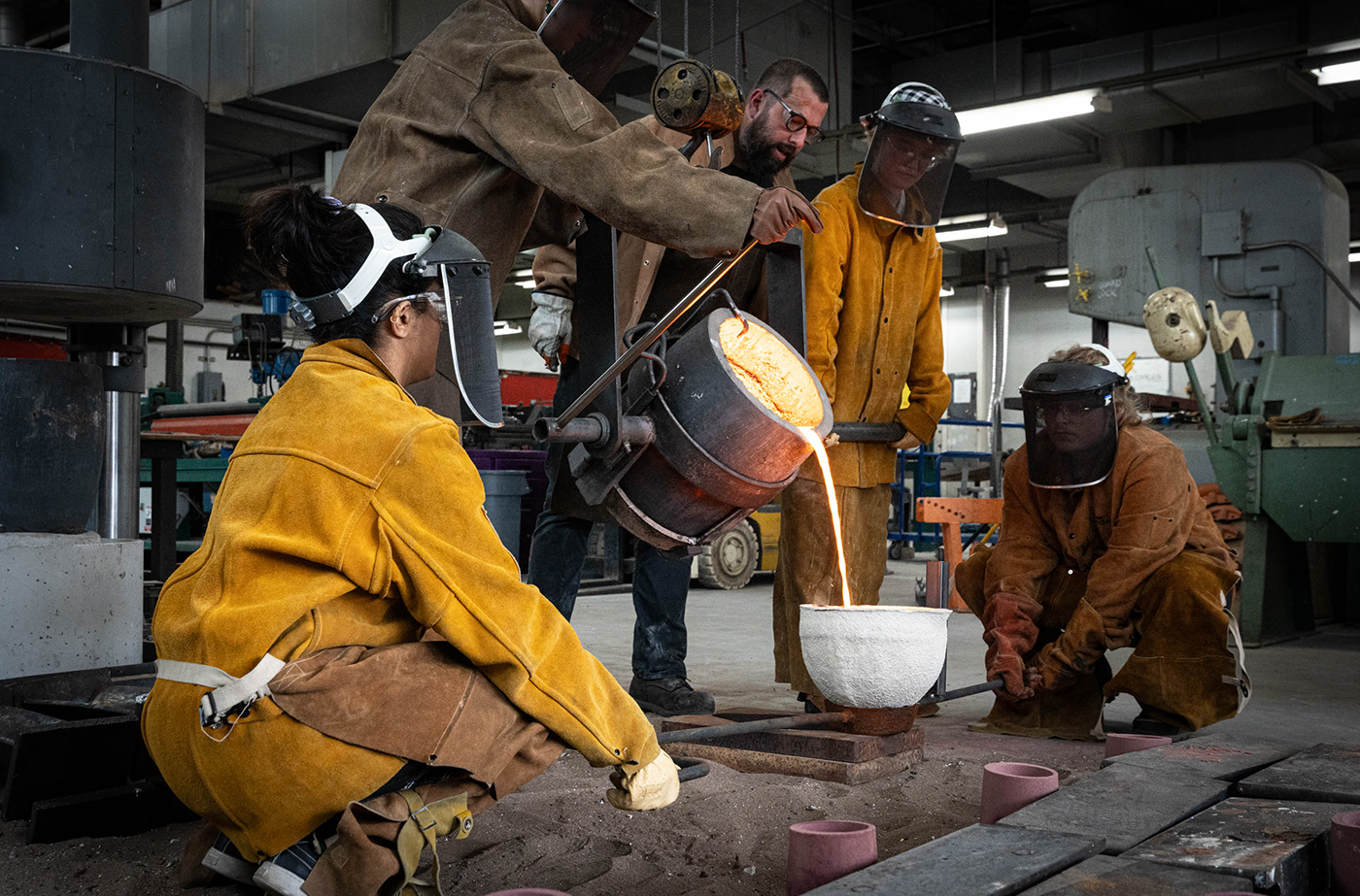 Lucy Tansey and Jules Frank pour molten bronze into a ladle (held by Asthana and Foreman).