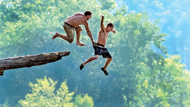 two men jumping into a river from a rock