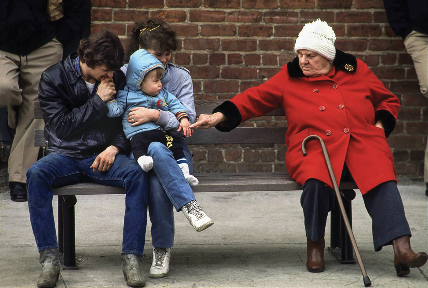 an old woman and a young family sit at the bus stop