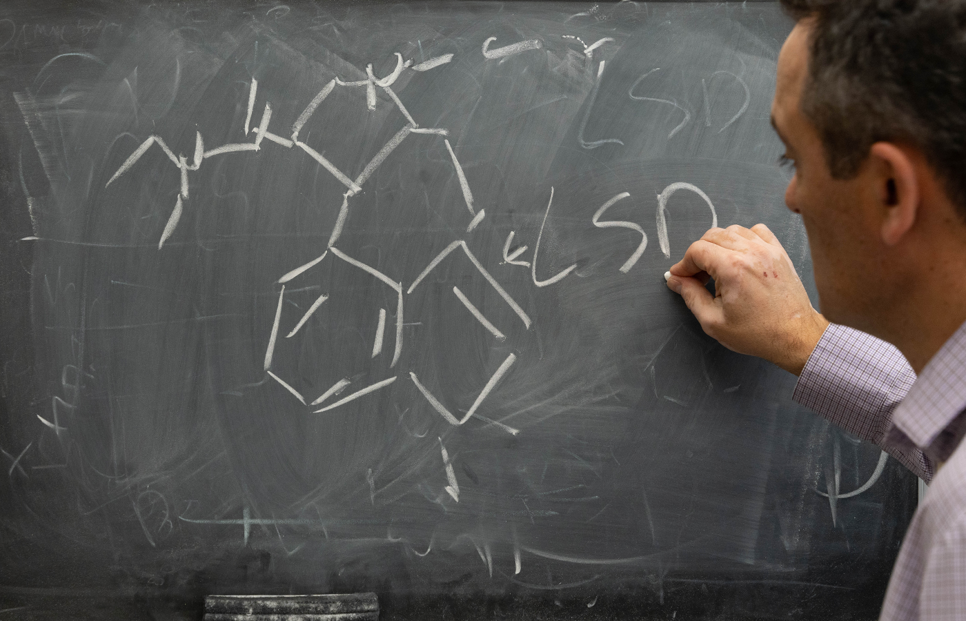 A professor diagrams a chemical compound on a chalkboard